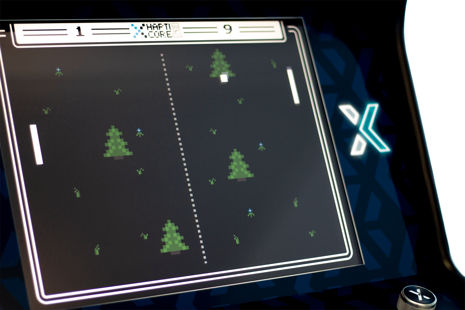 The image shows a close-up of the HAPTICORE Arcade screen with 8-bit pixel graphics of trees, a ball, and a cursor. The cursor is controlled by a HAPTICORE rotary haptic actuator. The haptic feedback varies depending on the background and changes every few seconds.