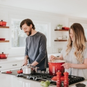 The picture shows a couple preparing a dish together at the stove in the kitchen.