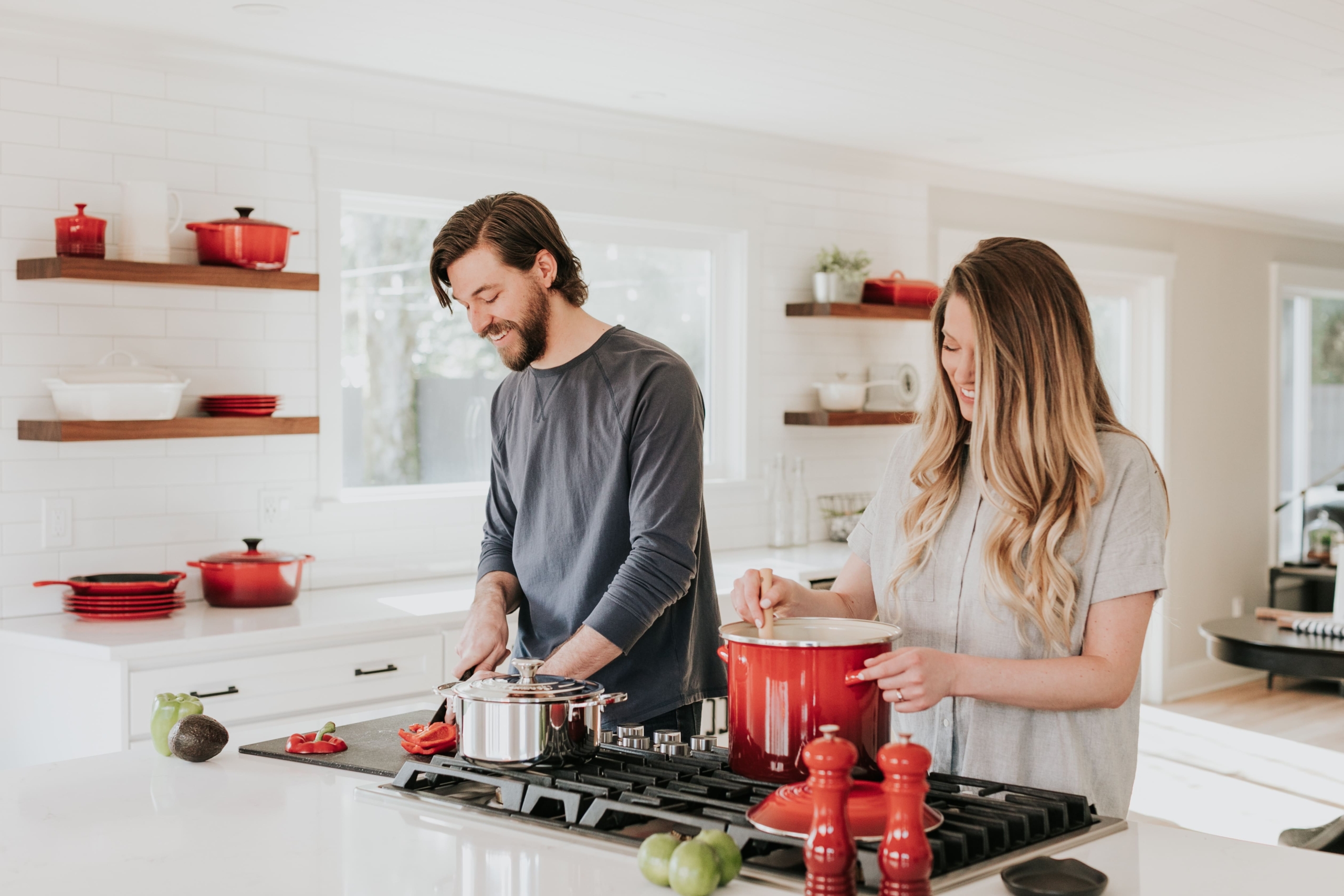 The picture shows a couple preparing a dish together at the stove in the kitchen.