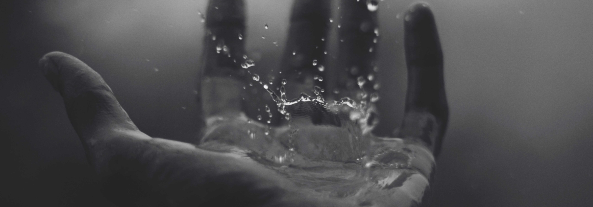 Image of waterdrops falling onto an outstretched hand.