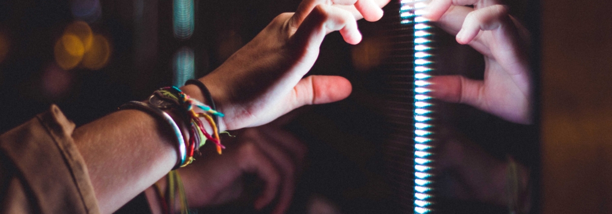 The image shows a hand in the dark touching a bright reflective surface with a strip of glowing LEDs.