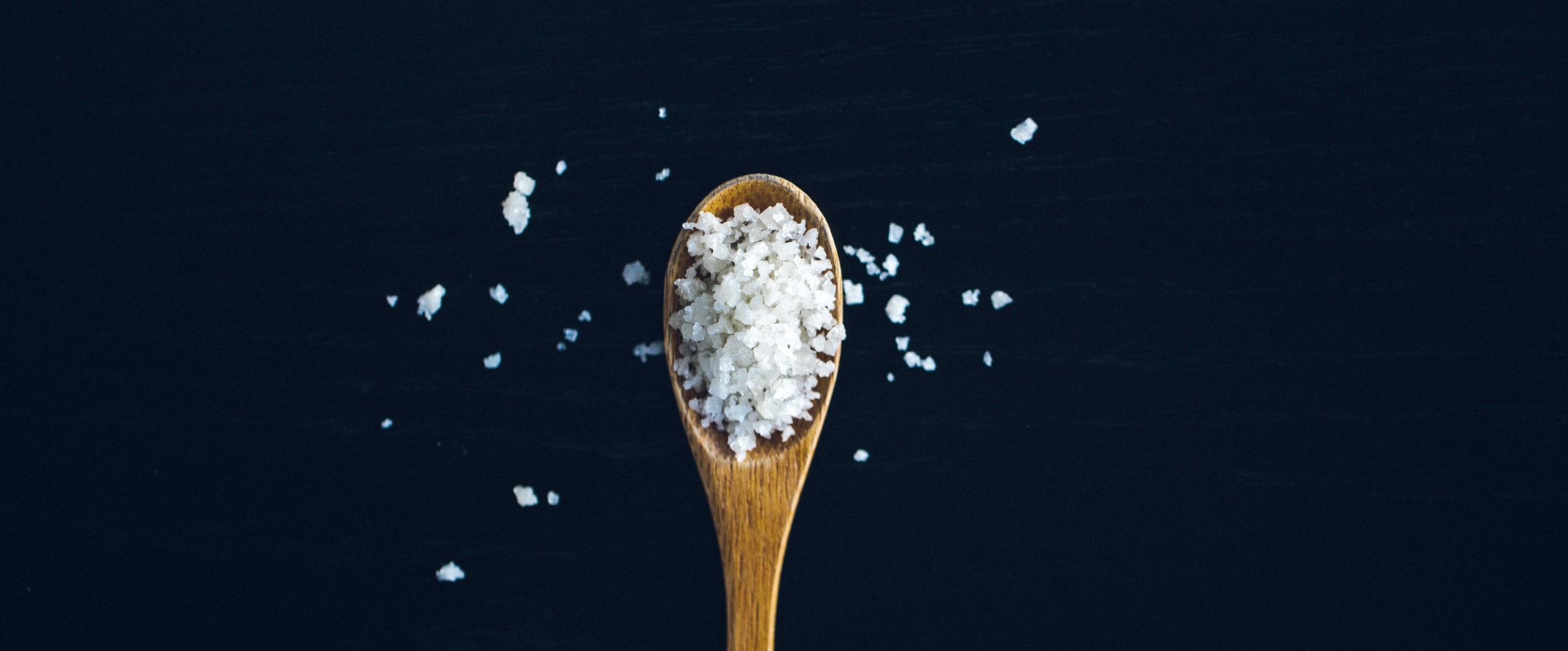 The image shows a cooking spoon with rough salt on a dark countertop. The salt represents haptics in HMIs, which, like in a dish, spices up the user experience.